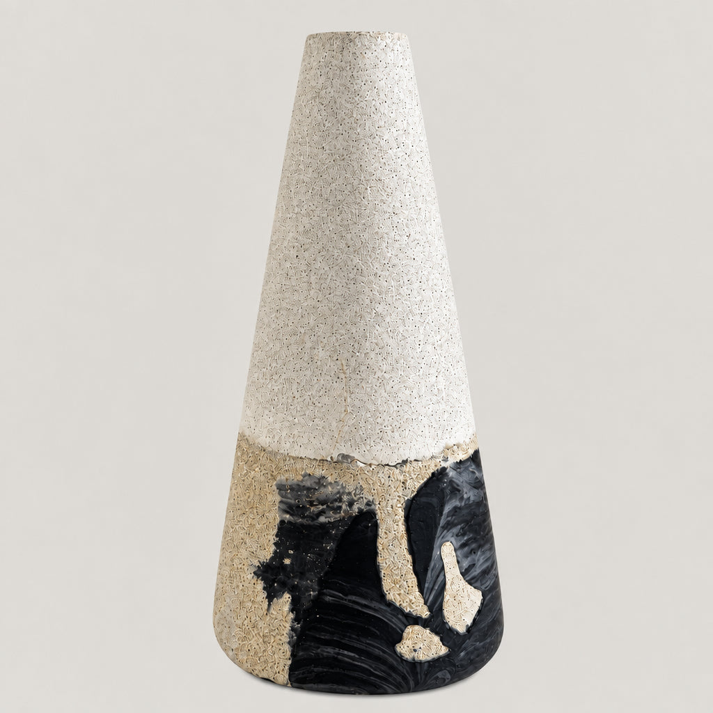 A handmade ceramic cone vase with a textured light gray upper half and a marbled black, white, and beige lower half, standing on a white surface against a neutral gray background.