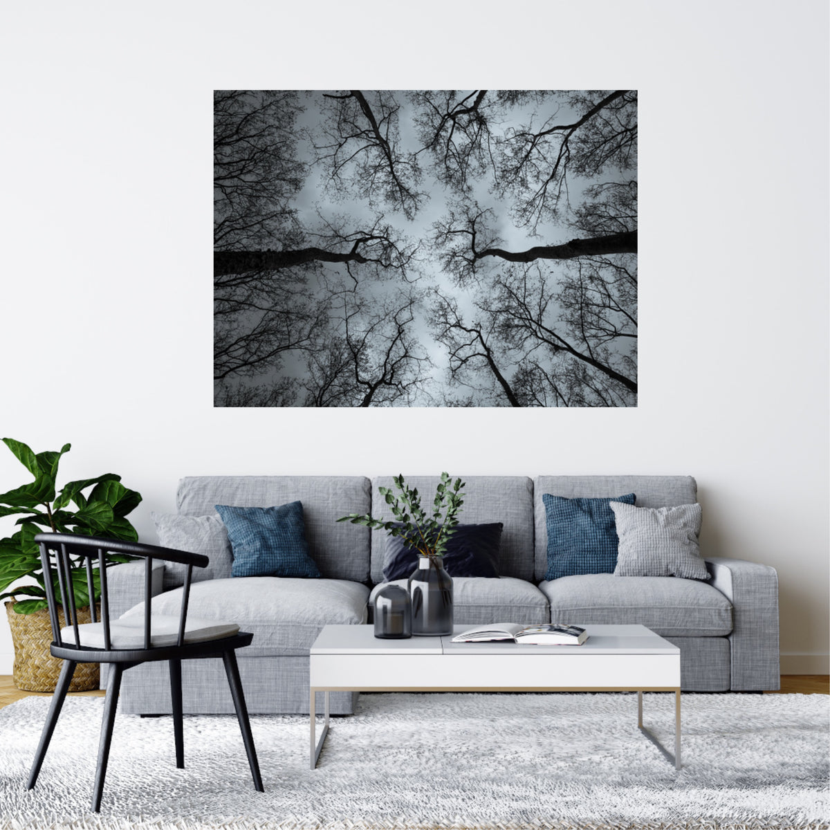 A large square wall art print showing a black-and-white tree canopy viewed from below, displayed above a light gray sofa in a modern living room setting.